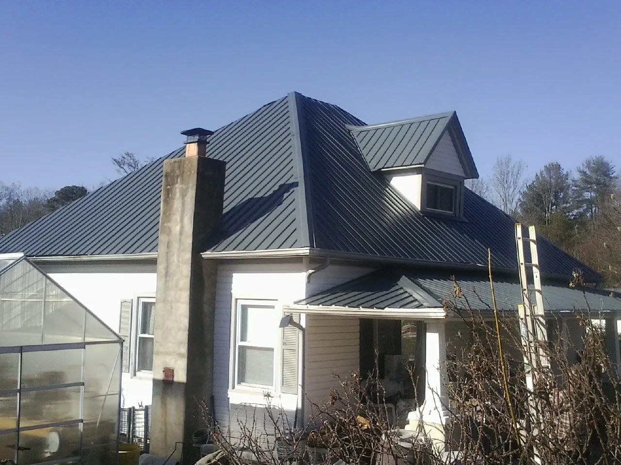 Dark blue standing seam metal roof on a white farmhouse with dormer — Slate & Tile Roof Repair by Roofing Brothers in East Amherst