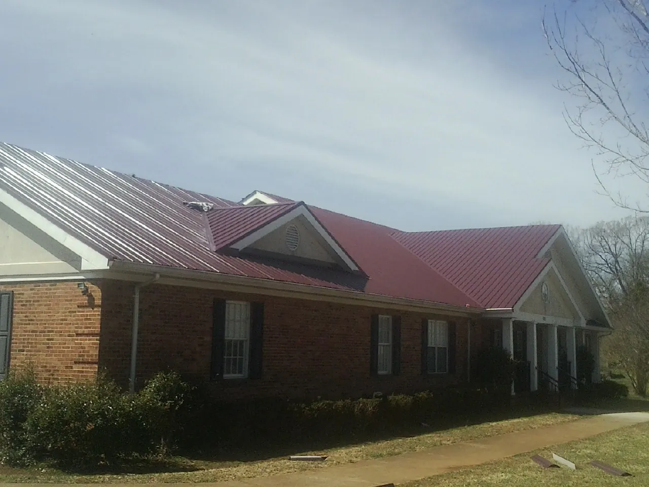 Red metal roof with gabled entries on a long brick building, from a Hail Damage Roof Repair job in East Amherst