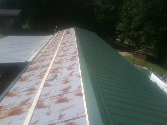 Old rusted panels beside newly installed green metal roofing — Wind Damage Roof Repair by Roofing Brothers in East Amherst