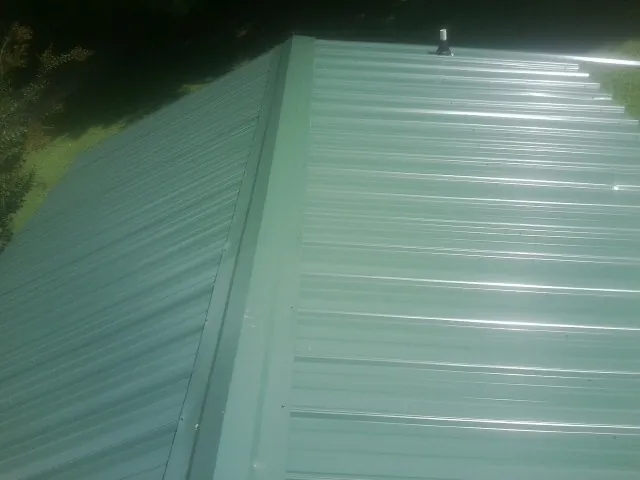 New green metal panels meeting at the ridge of a roof — Flat Roof Repair work by our crew in East Amherst