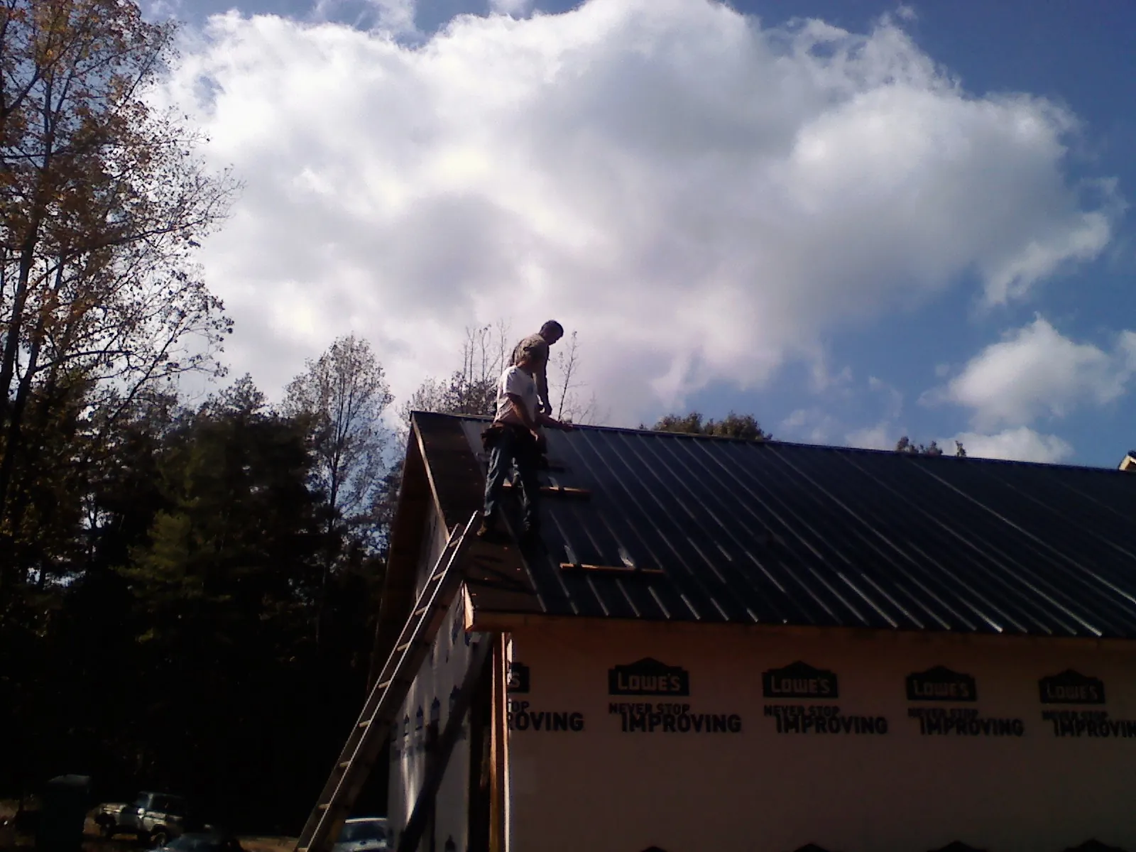 Roofer fastening dark metal panels high against a cloudy sky, from a Roof Inspection job in East Amherst