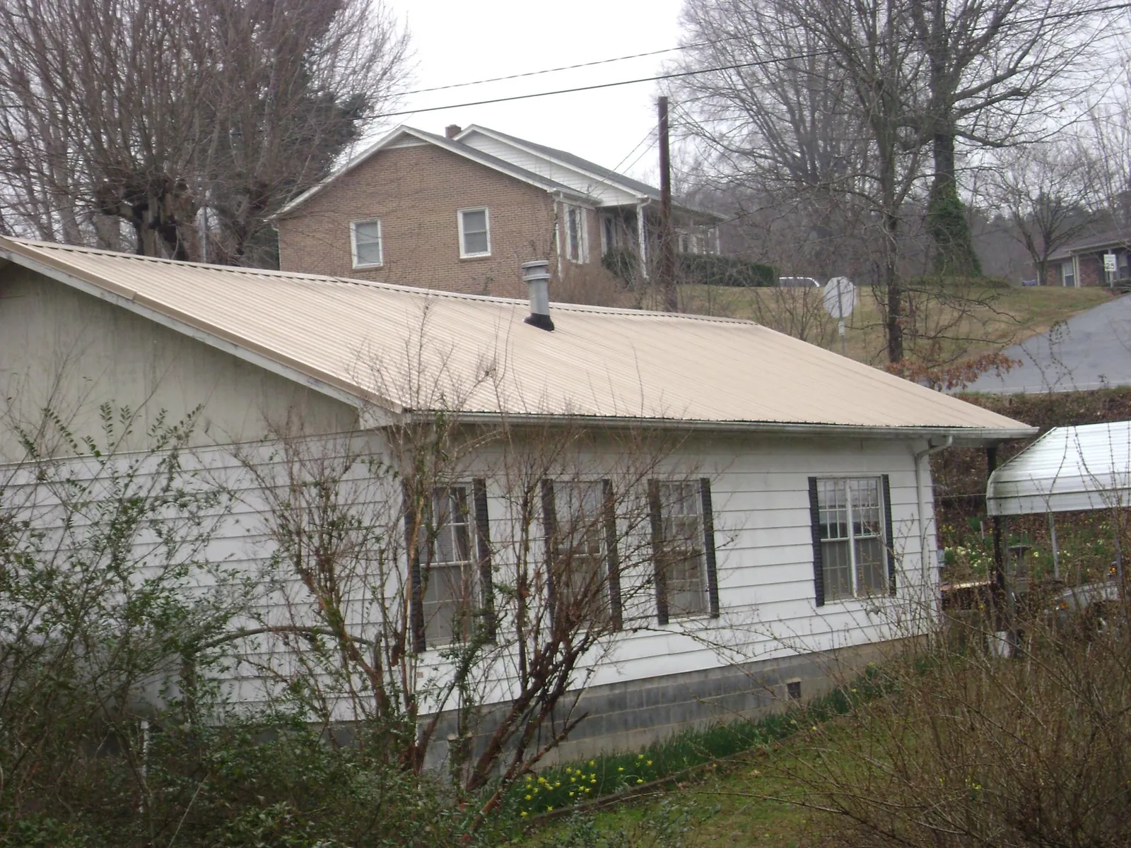 Tan metal roof on a white sided house set into a hillside — Commercial Roofing by Roofing Brothers in East Amherst