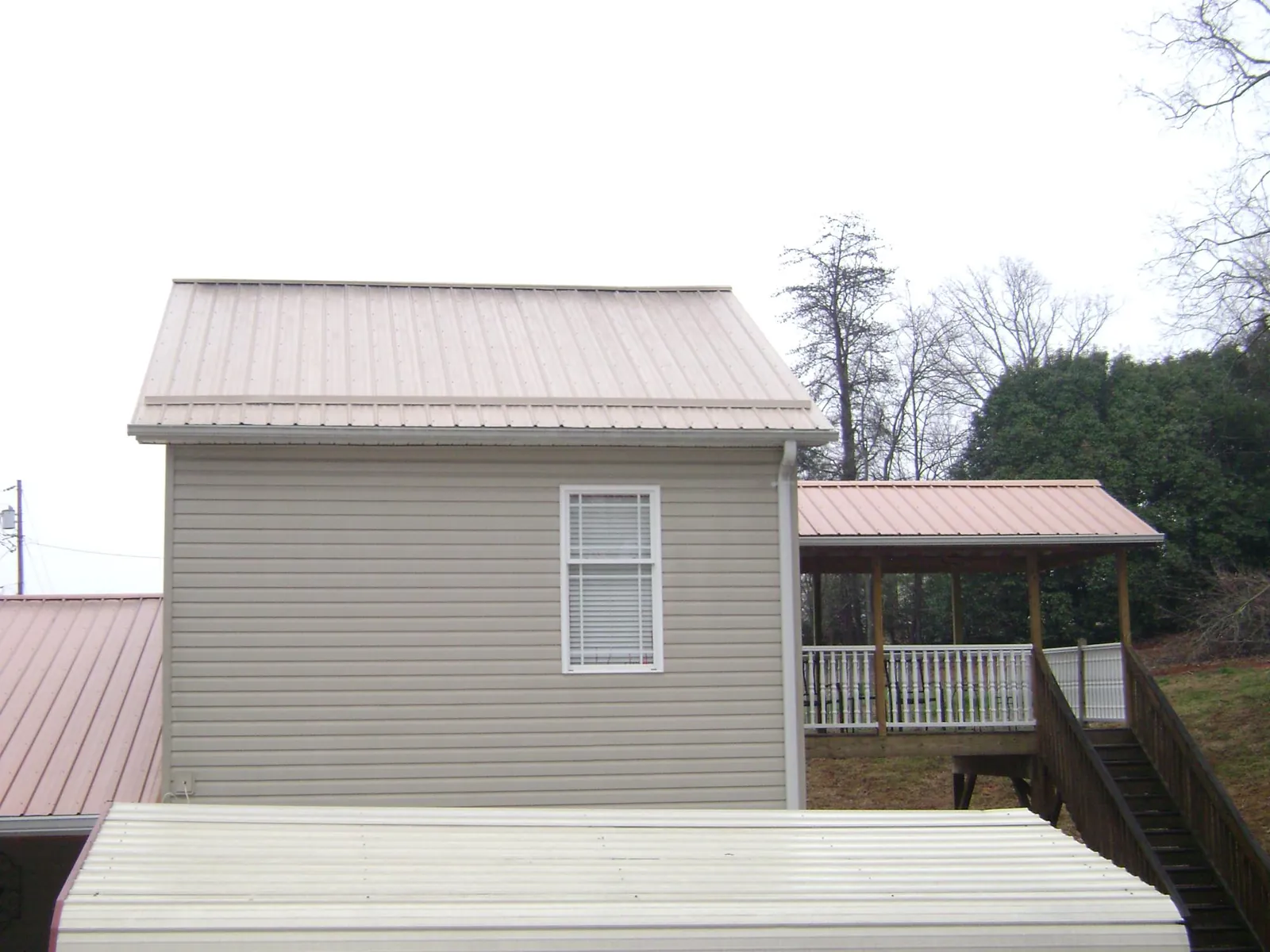 Tan metal roofs on a two story addition and attached porch, from a Roof Replacement job in East Amherst